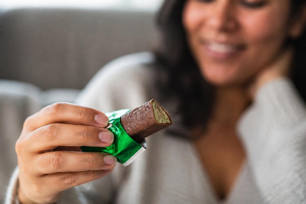 Peppermint Crisp chocolate bar with a bright green wrapper, partly unwrapped to show its brown, textured centre.