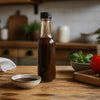 Worcestershire sauce in a clear glass bottle with dark brown liquid and a black cap, beside a dipping bowl; Worcestershire Sauce NZ