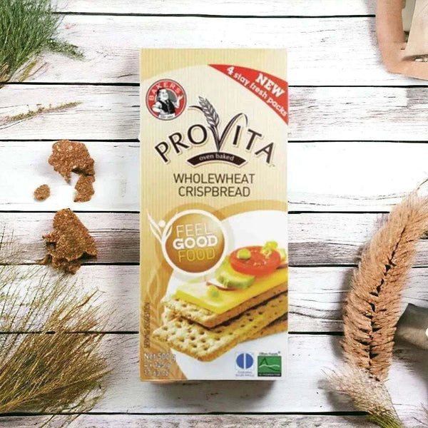 Bakers Provita Wholewheat Crispbread 500g box on a rustic wooden table with scattered crispbread pieces.
