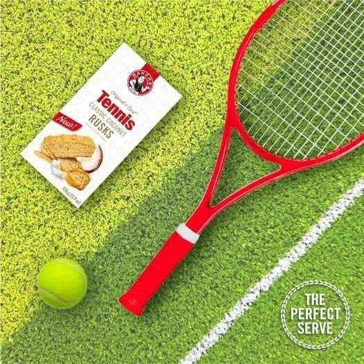 Bakers Tennis Classic Coconut Rusks 450g pack on grass with tennis racket and ball.