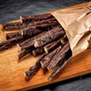 Bundle of traditional South African dry wors sticks spilling out of a brown paper bag on a wooden cutting board