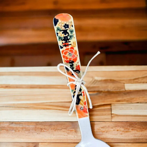 Enamel printed sugar spoon with colorful floral handle and wooden painted design tied with white string