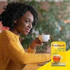 Woman enjoying a cup of Freshpak Rooibos Tea with a box of 40 tagless teabags on a table