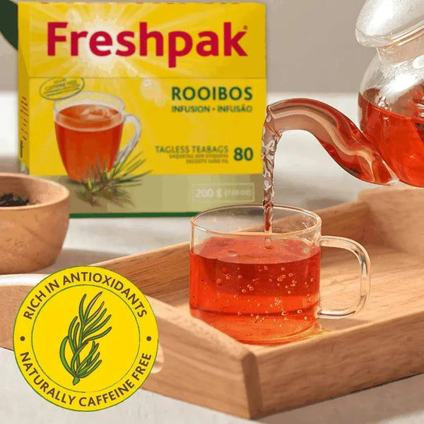 Freshpak Rooibos Tea 80's box with tea being poured into a clear glass cup on a wooden tray, highlighting natural caffeine-free antioxidant-rich infusion.