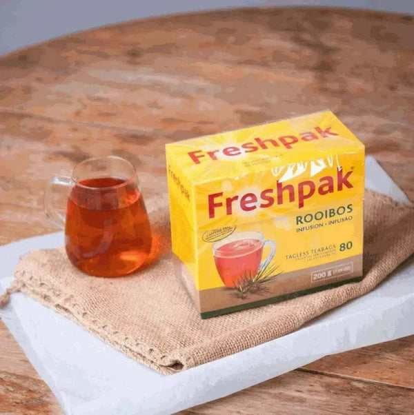 Freshpak Rooibos Tea 80's box with a glass cup of brewed rooibos tea on a wooden table