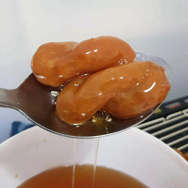 Close-up of two golden brown Koeksisters dripping with sweet syrup on a spoon above a bowl