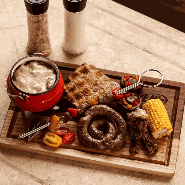Traditional 3-legged cast iron pot with rustic meal, featuring sausage, corn, and grilled bread on a wooden board.