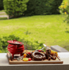 Traditional 3-legged red enamel cast iron pot with lid, surrounded by barbecue food, perfect for outdoor cooking.