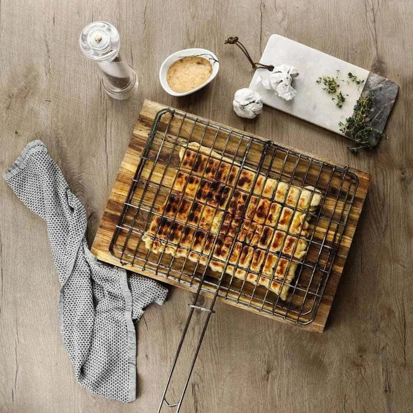Stainless steel braai grid with cooked food on wooden board and kitchen accessories on wooden surface
