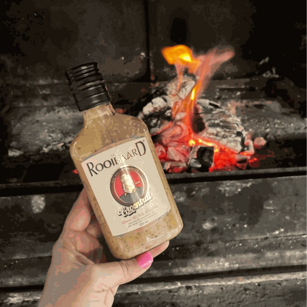 Rooibaard Groen Trui Chilli Sauce bottle held near a glowing barbecue fire.