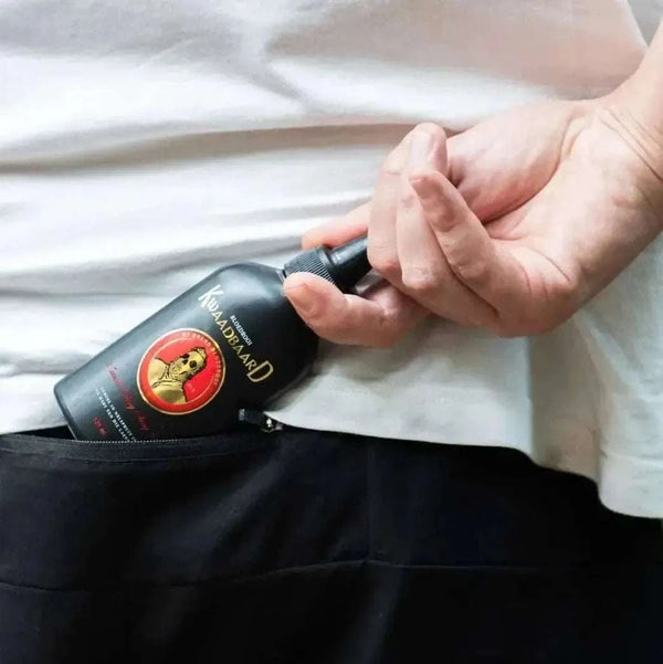 Person placing a bottle of Rooibaard Kwaadbaard Sauce in a pocket, showcasing portability.