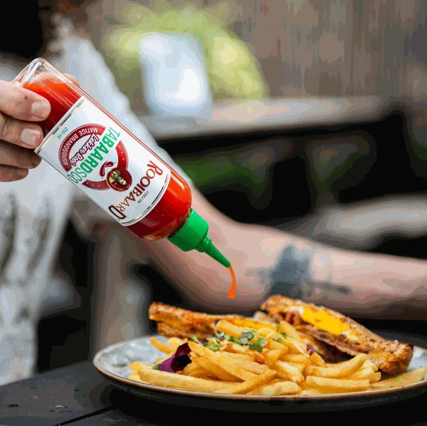 Rooibaard Tabaardsco Rooi Sauce being poured onto fries and chicken, showcasing its vibrant red color and easy squeeze bottle.