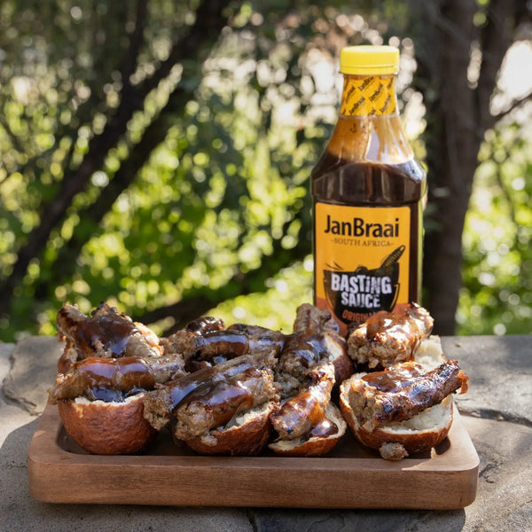 Jan Braai Basting Sauce bottle with grilled meat sliders topped with barbecue sauce on wooden board outdoors