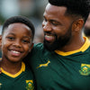 Springbok Jersey in dark green fabric with gold V-neck trim, yellow logos and crest, worn by a man and boy