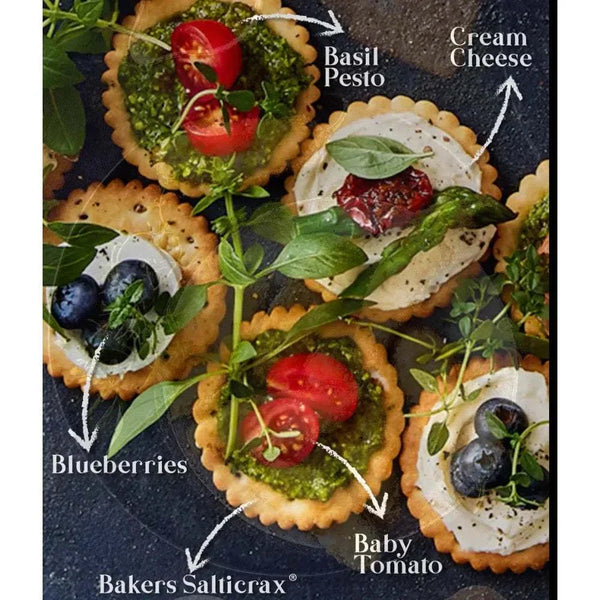 Bakers Salticrax Salted Crackers topped with cream cheese, basil pesto, blueberries, and baby tomato.