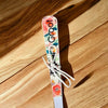 Enamel printed sugar spoon with floral design and wooden painted handle on wooden surface