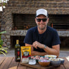 Jan Braai Classic Oxtail Potjie Sauce 400g pouch with cooking ingredients on wooden table outdoors
