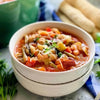 Minestrone soup in a white bowl with vegetables and herbs.