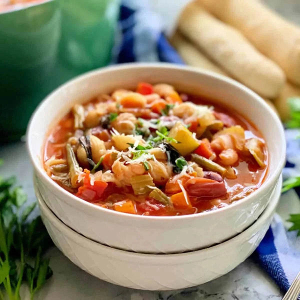 Minestrone soup in a white bowl with vegetables and herbs.