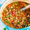 Colorful minestrone soup with pasta and vegetables in a blue pot.