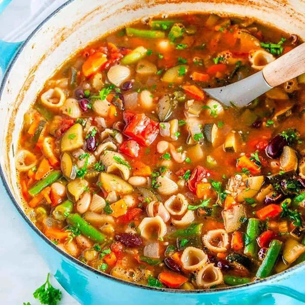 Colorful minestrone soup with pasta and vegetables in a blue pot.