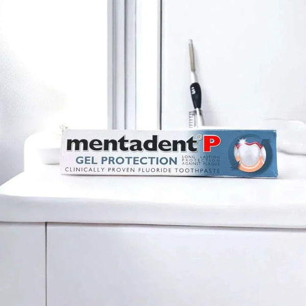Mentadent P Gel Protection toothpaste tube on a white sink with a toothbrush in the background.