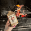 Rooibaard Groen Trui Chilli Sauce bottle held near a glowing barbecue fire.
