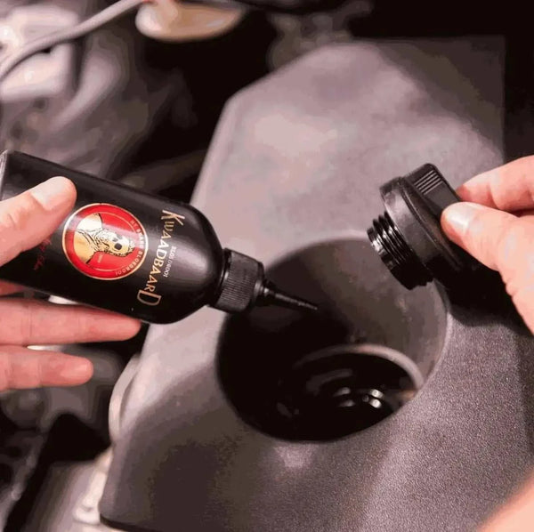 Rooibaard Kwaadbaard Sauce bottle being opened and held close to a container, showcasing its packaging and design.