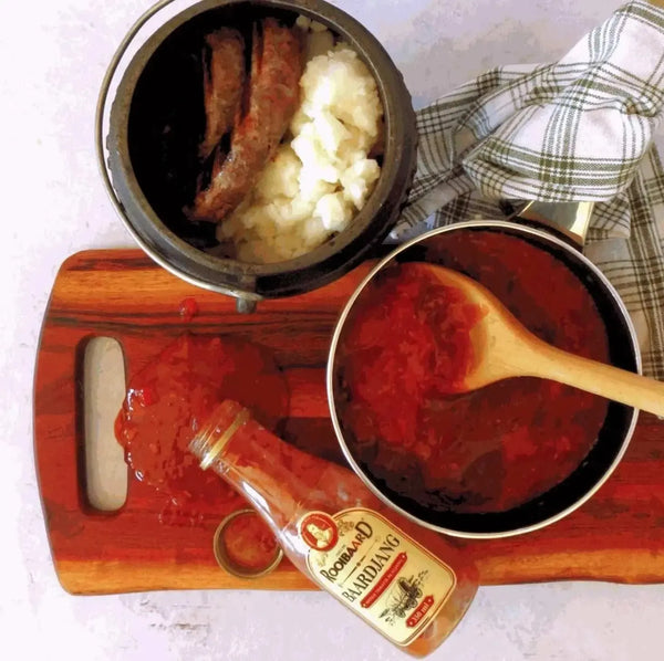 Rooibaard Sauce Baardjang Matige Tamatie alongside a dish, showcasing medium-spiced tomato sauce with sausages and potatoes.