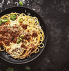 Plate of spaghetti topped with rich bolognaise sauce and garnished with fresh basil leaves and grated cheese