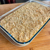Glass dish with creamy dessert topped with crumbled biscuits on a wooden surface.